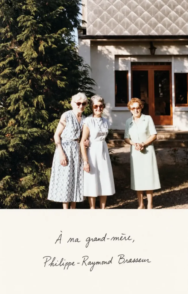 Trois femmes posent devant une maison. Sous la photographie figure la dédicace : « À ma grand-mère, Philippe-Raymond Brasseur ».